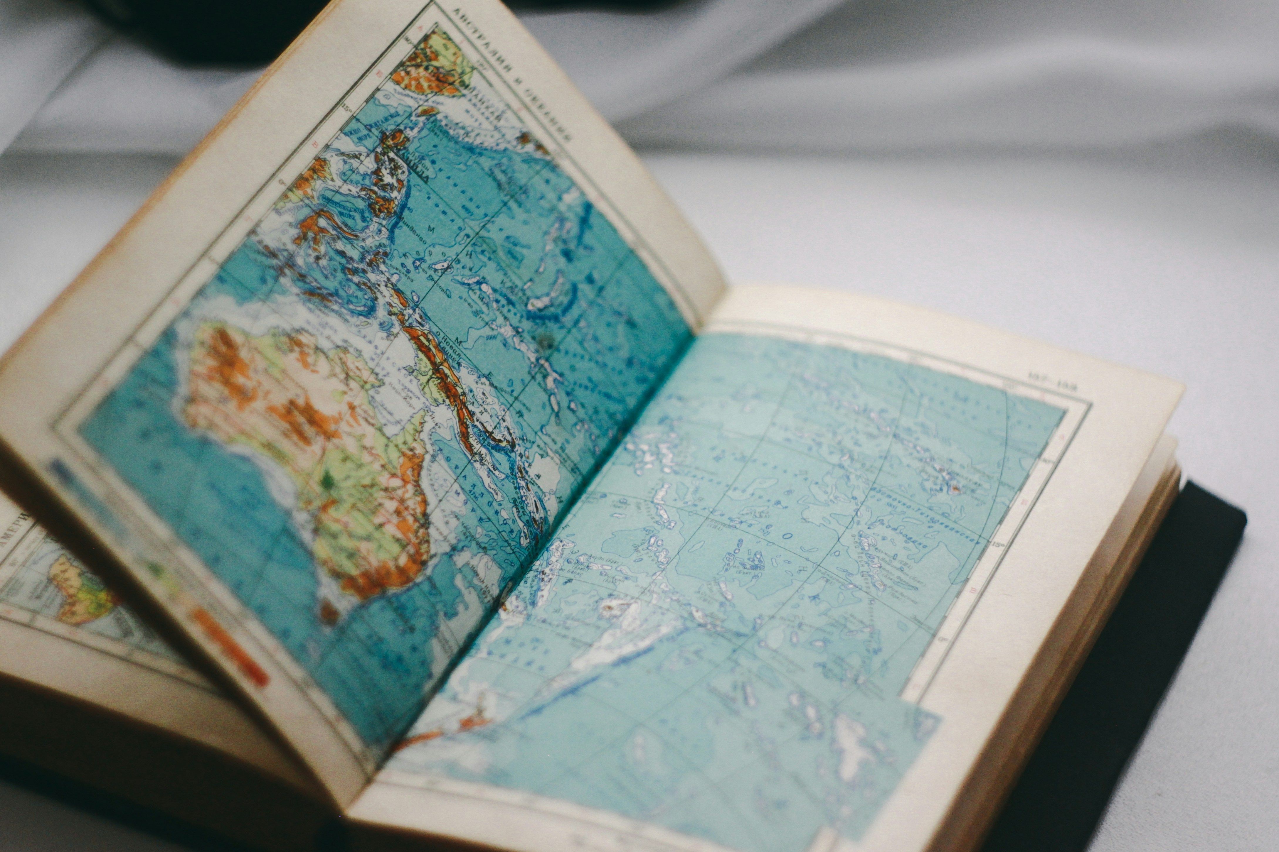 An open antique atlas, its hand-colored map pages catching soft light